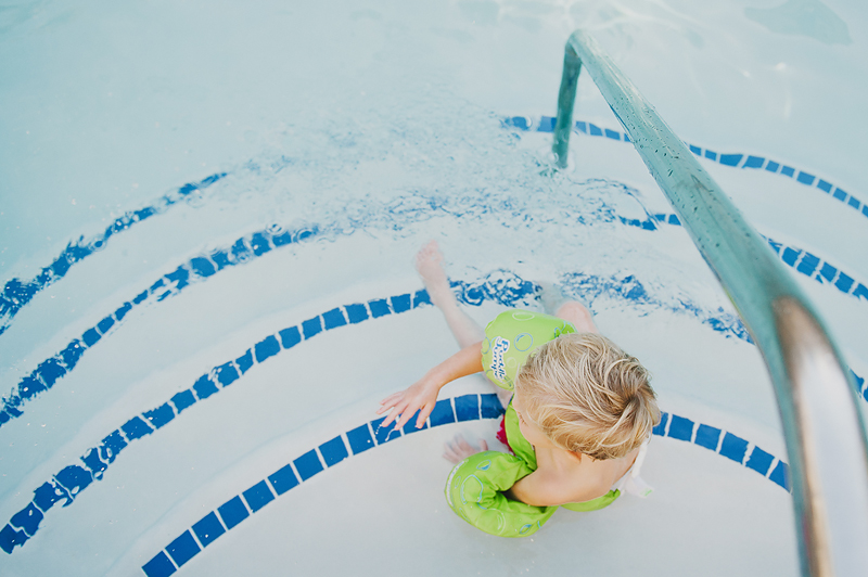 little boy sitting on steps of swimming pool in green lifejacket