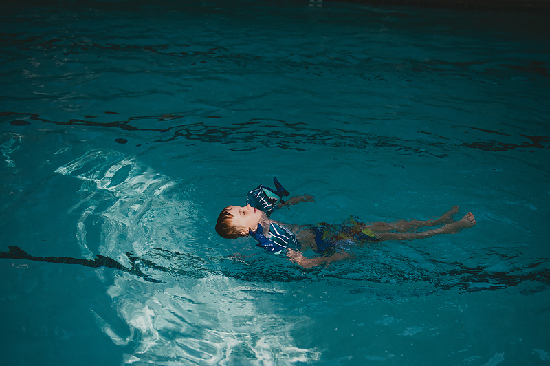 boy floating on back in swimming pool wearing shark floaties