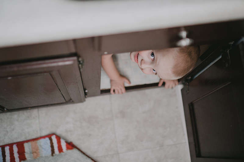 Toddler boy peeking out of bathroom cupboard