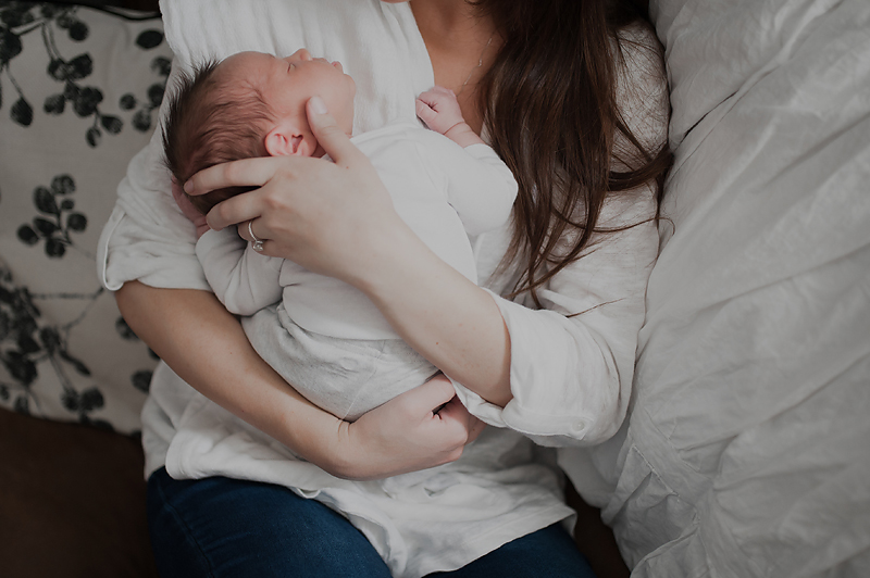Mom snuggling newborn baby boy on her shoulder while he sleeps