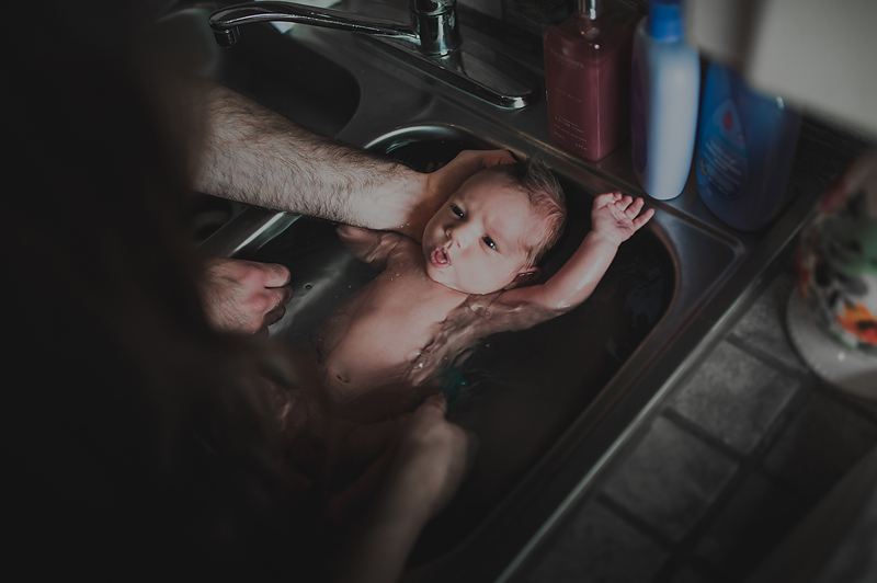 Mom and dad bathing newborn baby boy in sink