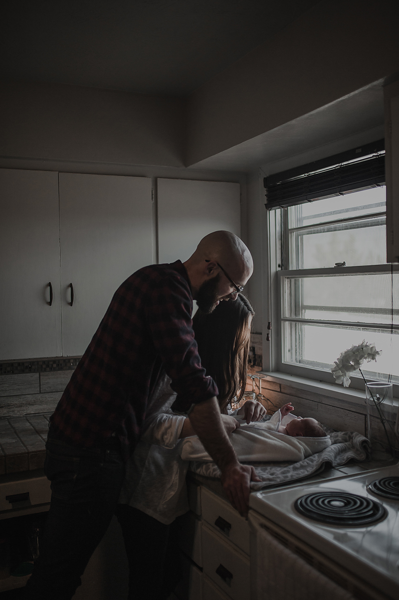 Mom and dad with newborn baby boy in towel next to window