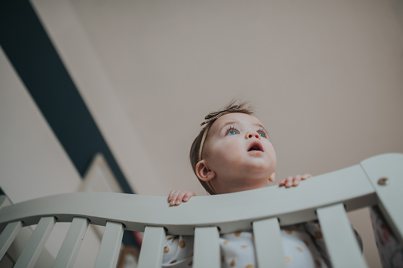 One year old baby girl in crib looking out the window