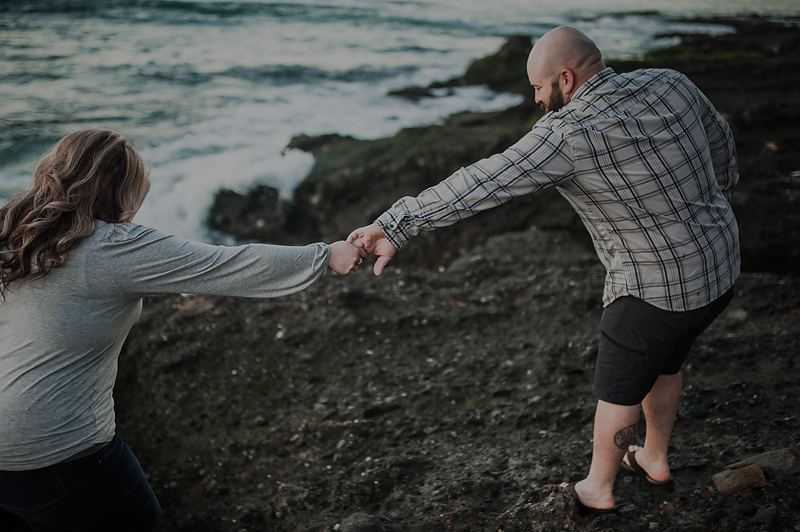 Couple helping each other on rocky beach in California.