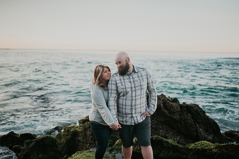 Couple on mossy green rocks overlooking the ocean.