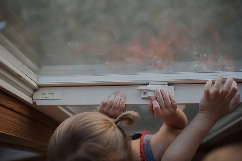 Baby girl with pigtails and big brother with fingers on windowsill