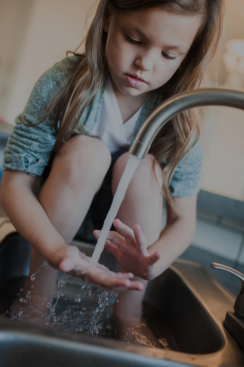 Little girl playing in the water at the sink