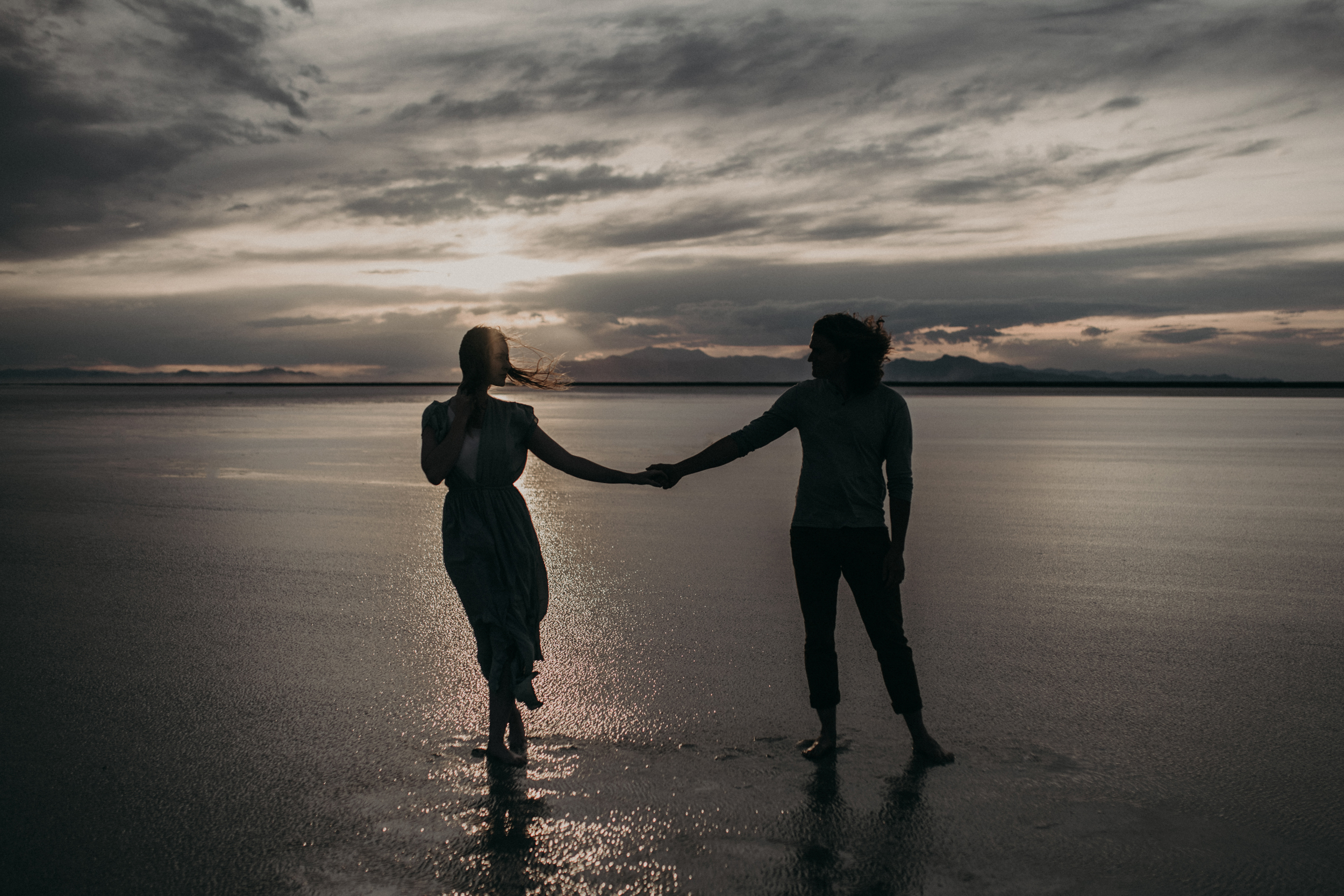 Silhouette of couple on water with mountains in background at sunset
