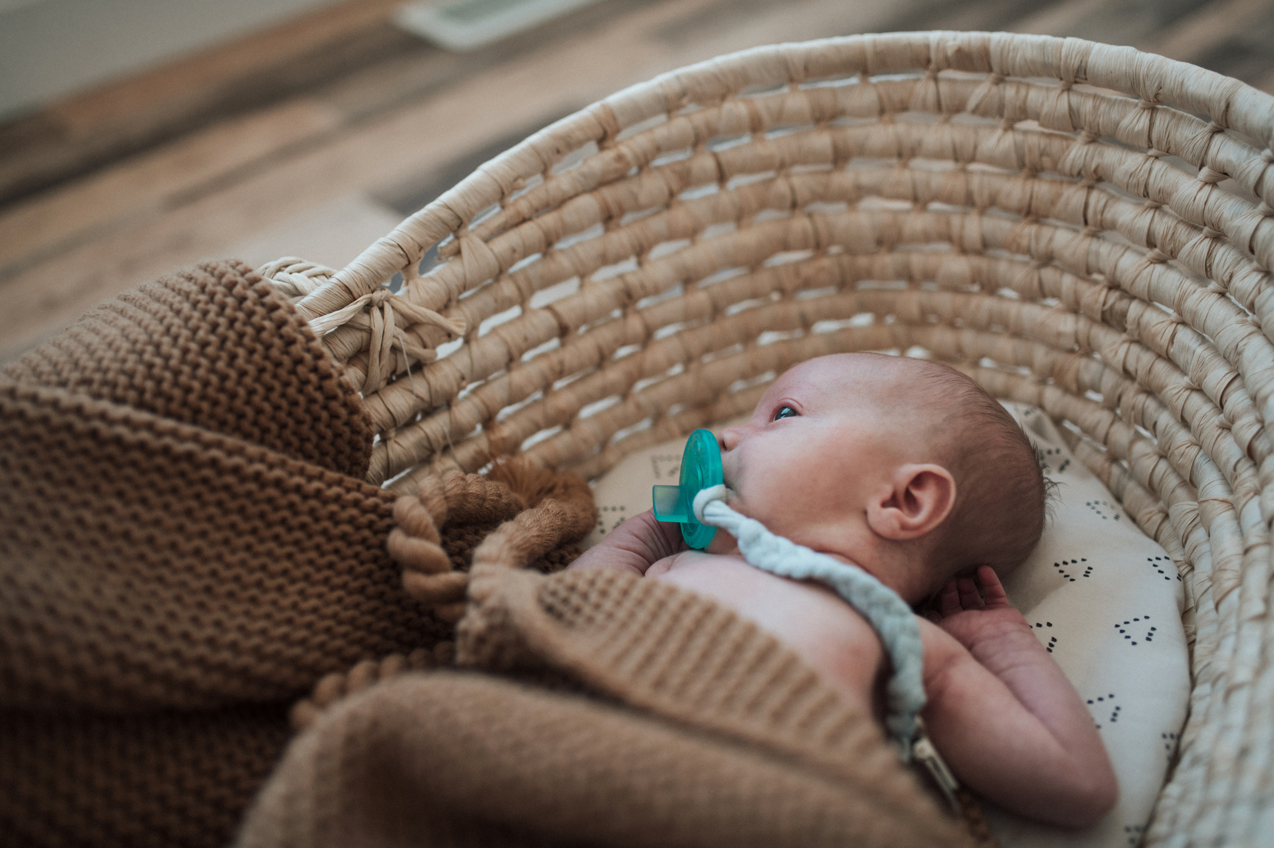 Baby boy lying in Moses basket sucking on binky brown blanket