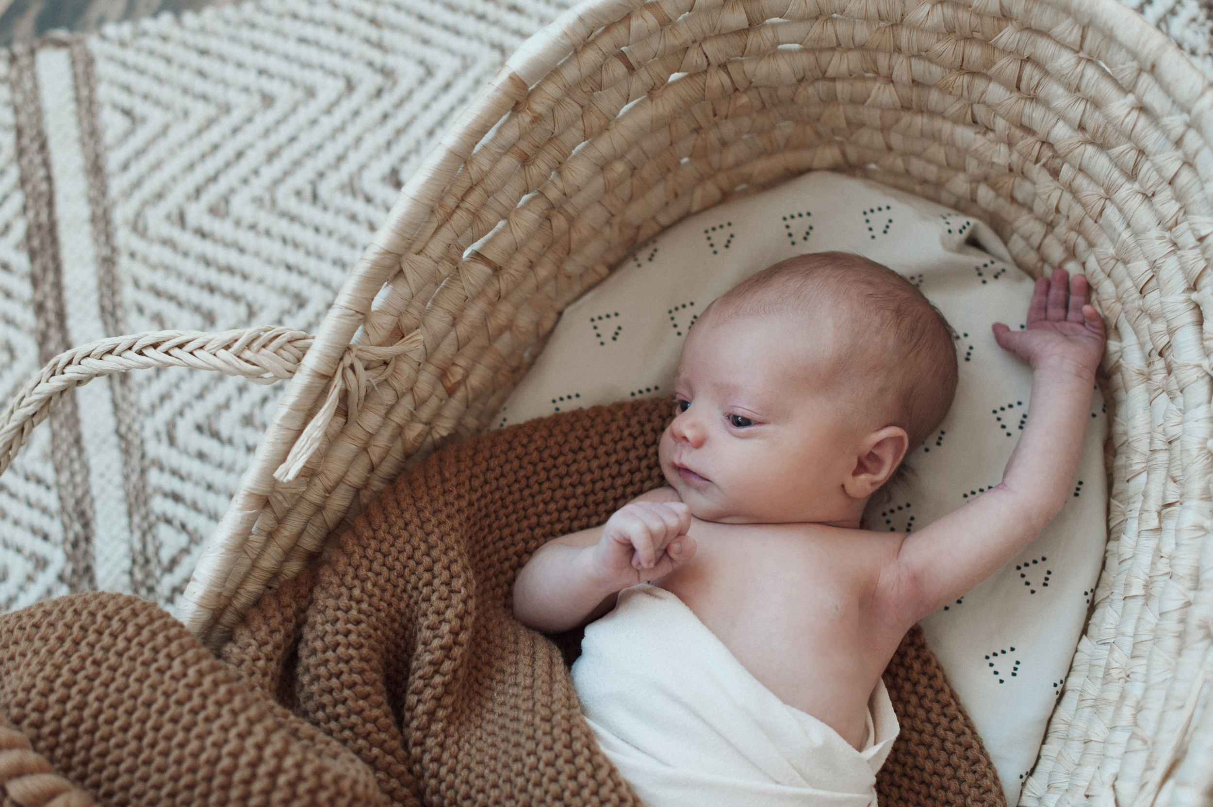 Baby boy stretching in Moses basket brown blanket