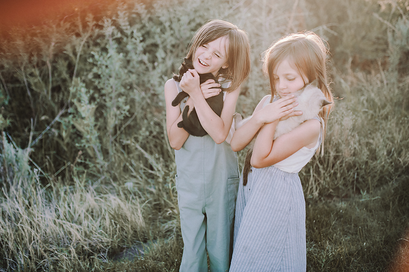 two girls holding kittens laughing in the sun