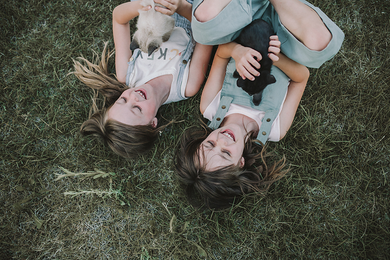 two girls lying on grass holding kittens laughing