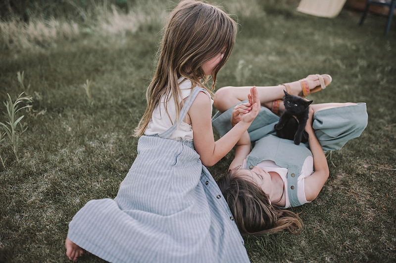 sisters holding hands on grass with black kitten