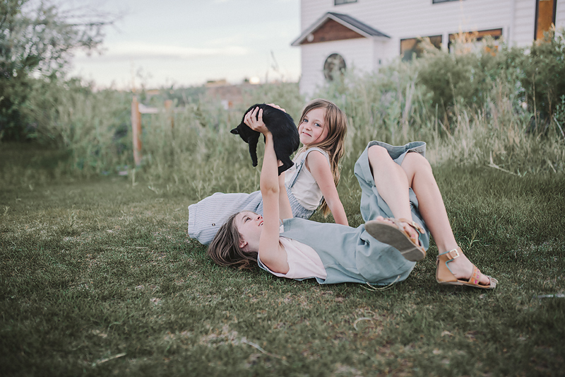 two girls lying on grass holding black kitten