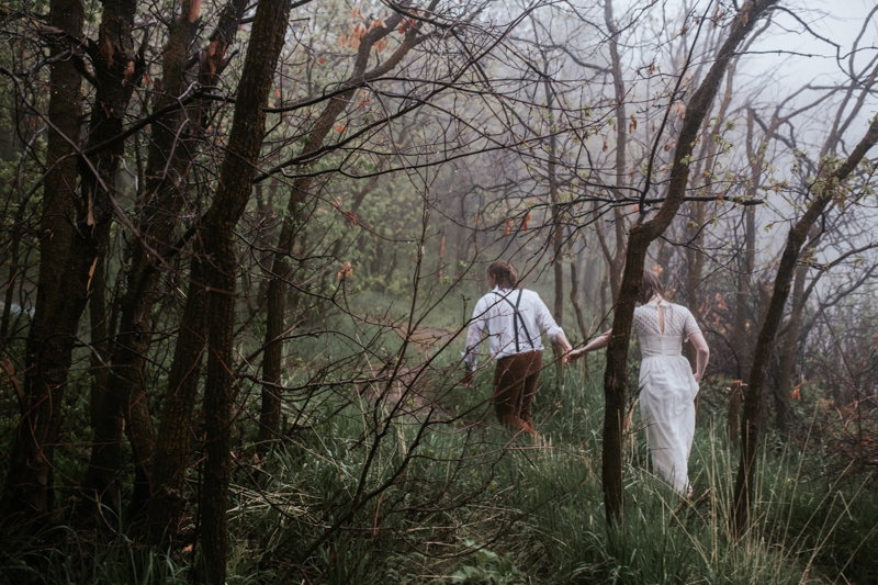 Couple running through trees in rain