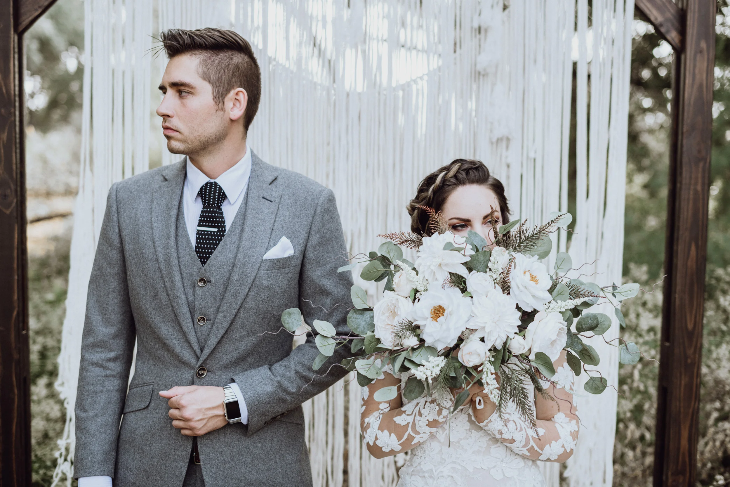 Bride holding bouquet with groom in front of macrame