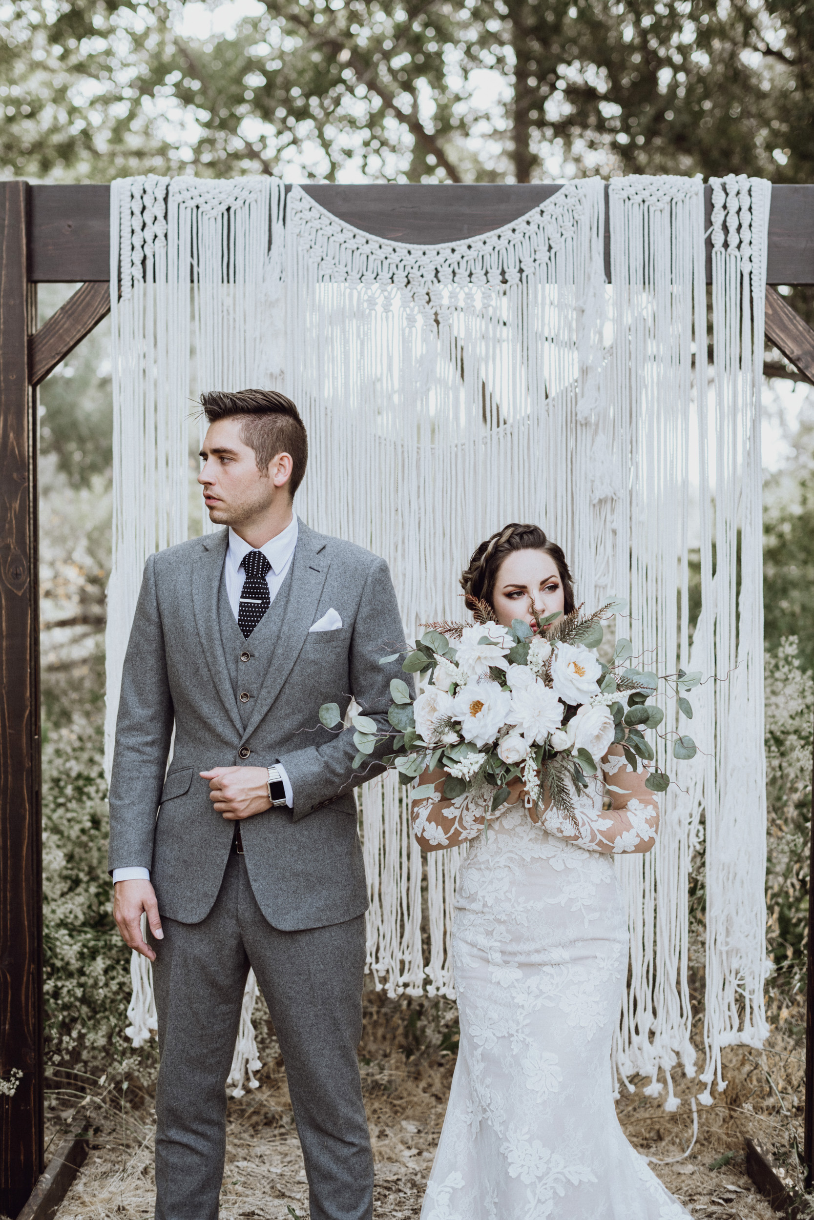 Bride holding bouquet with groom in front of macrame