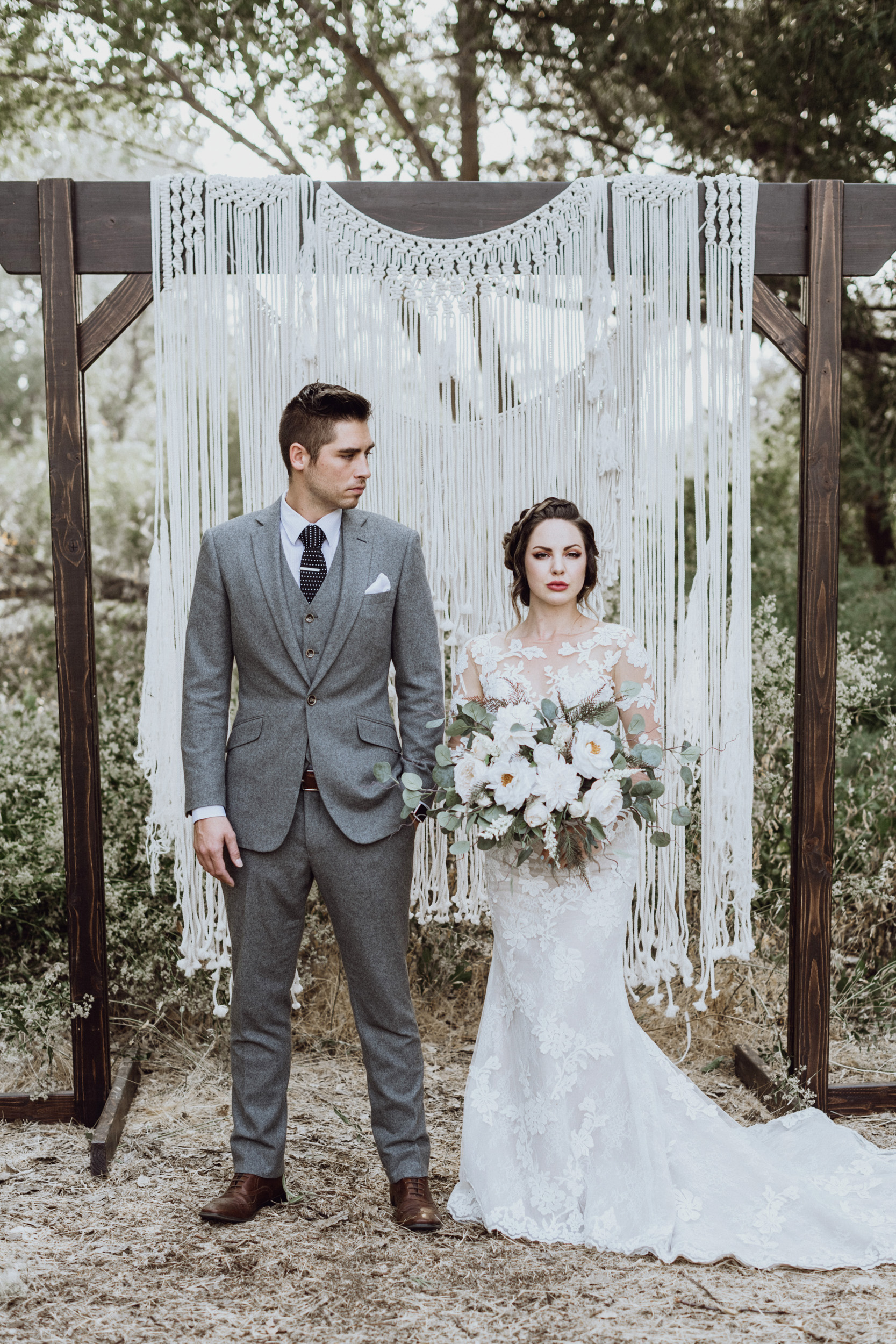Bride holding bouquet with groom in front of macrame