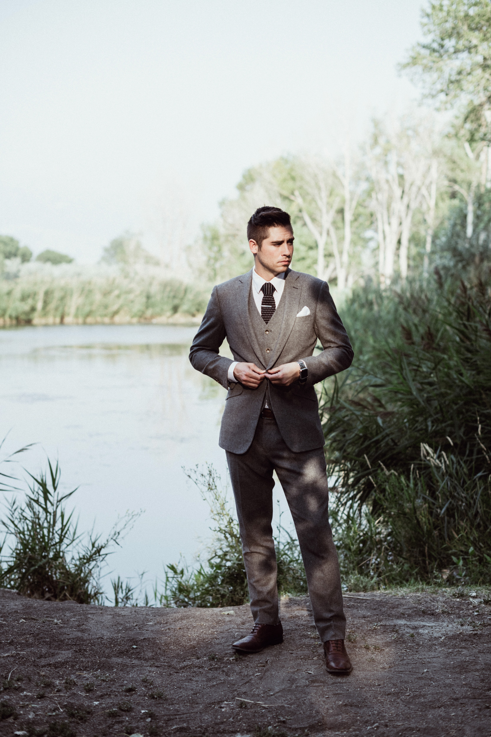 Groom in grey suit standing in front of pond 