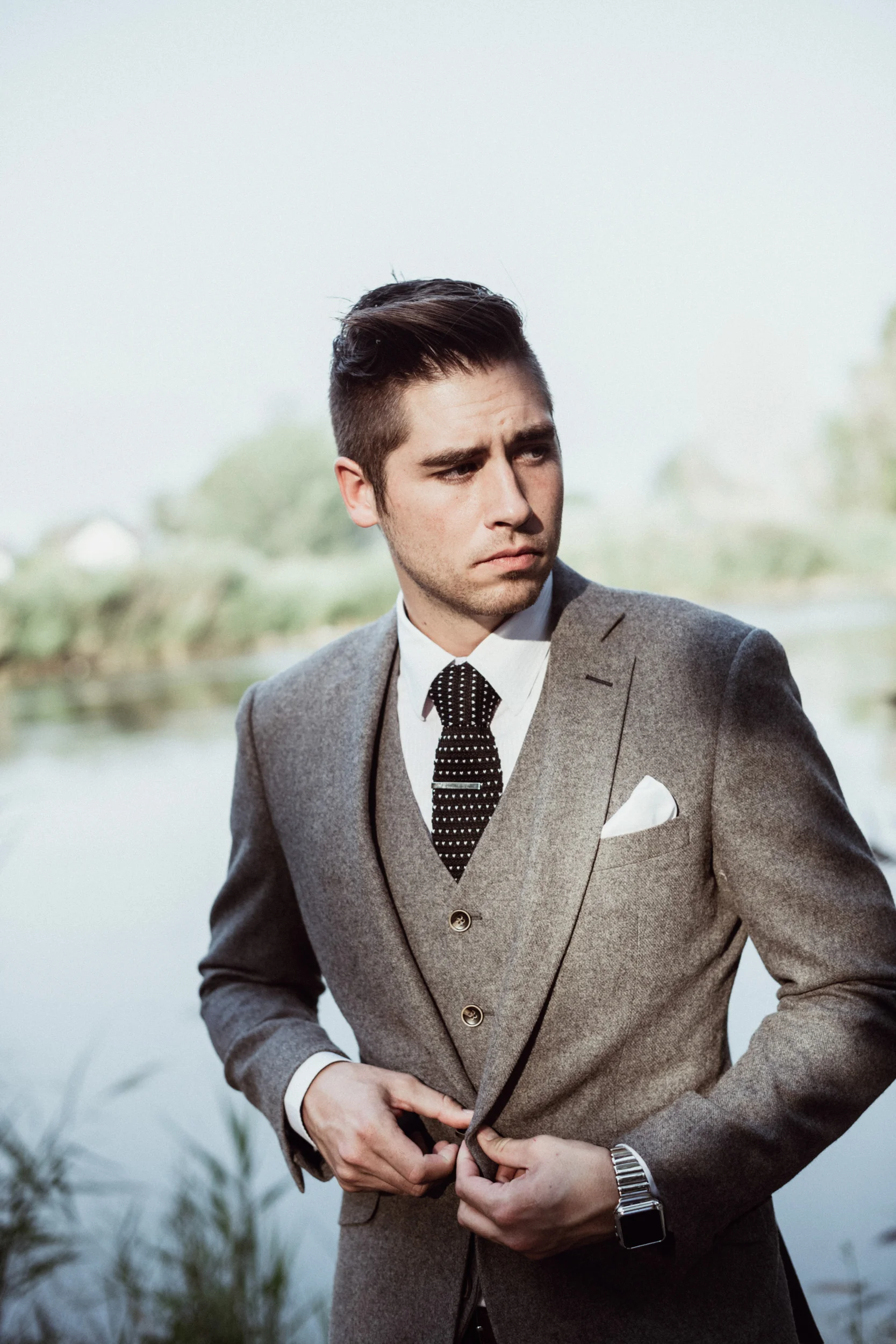 Groom in grey suit standing in front of pond