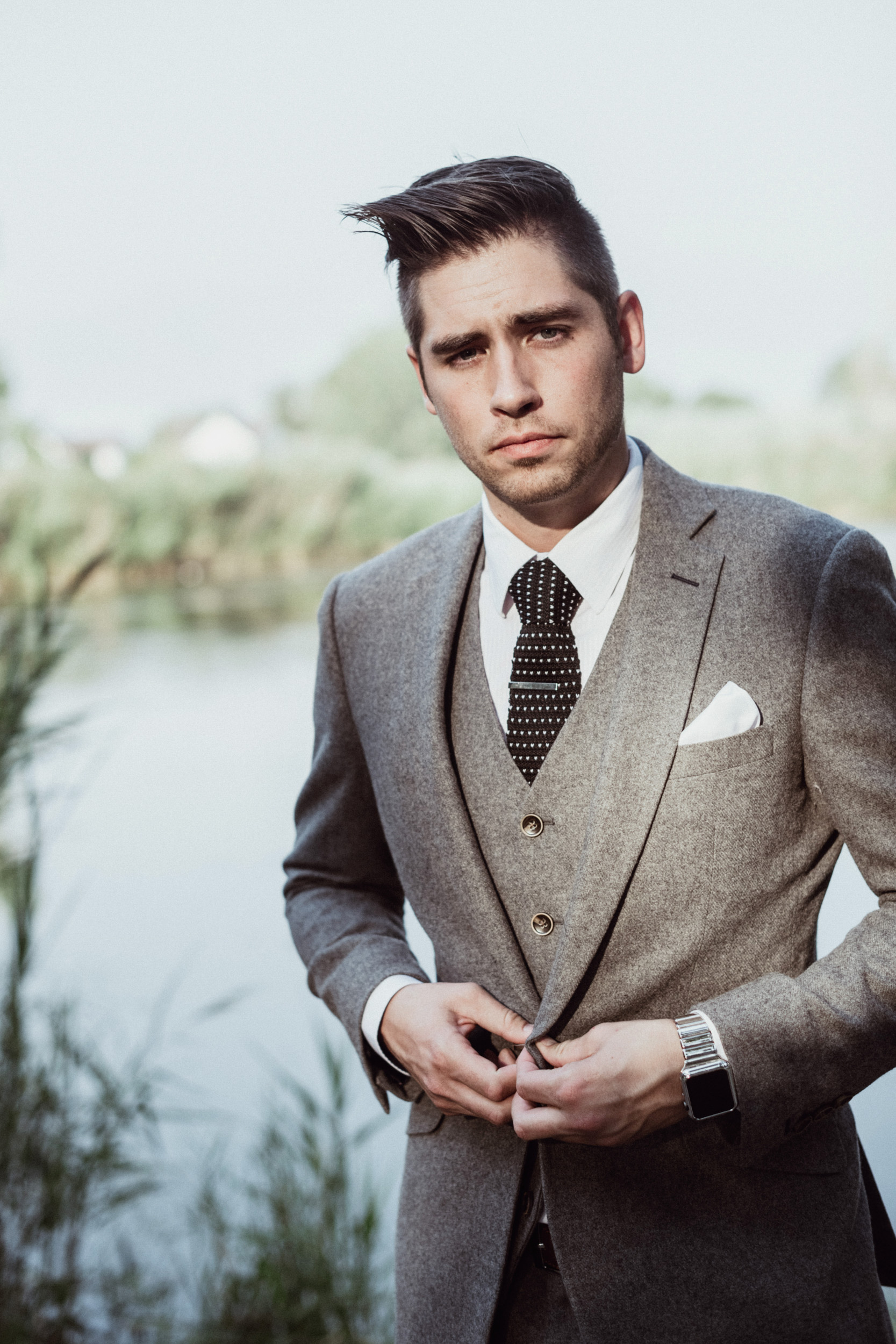 Groom in grey suit standing in front of pond 