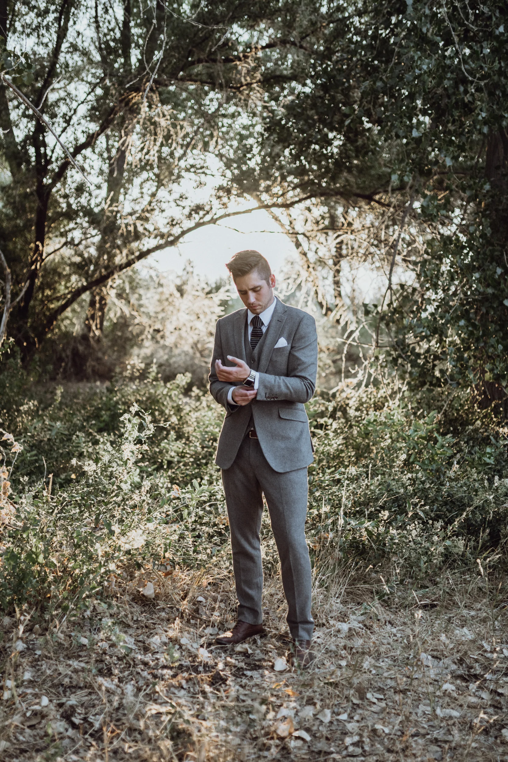 Groom in grey suit standing in grassy field