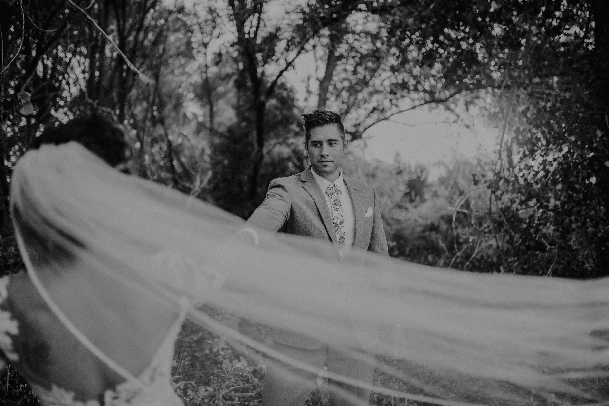 Groom looking at bride with a vail in a grassy field