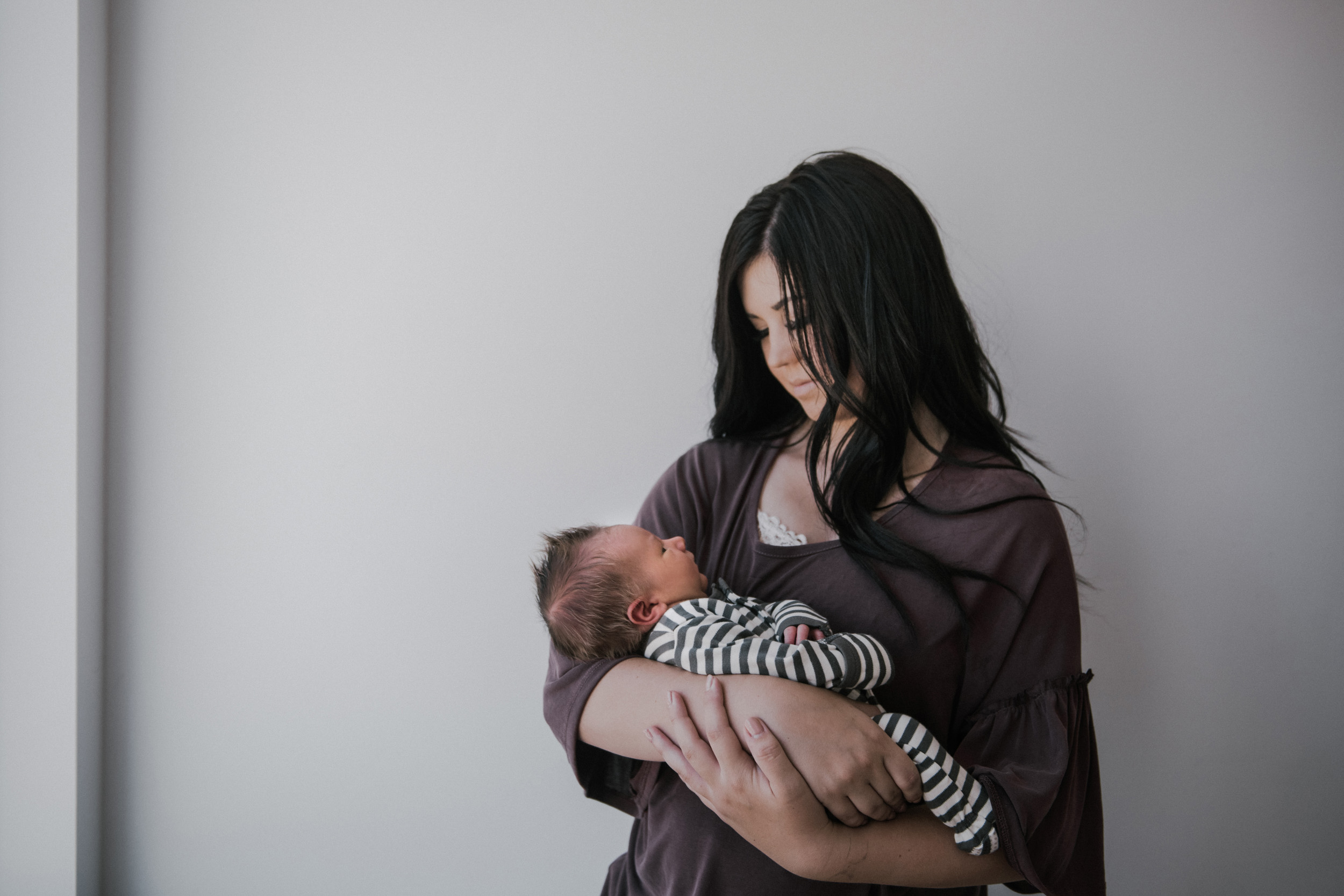 newborn boy in striped onesie being held by mom