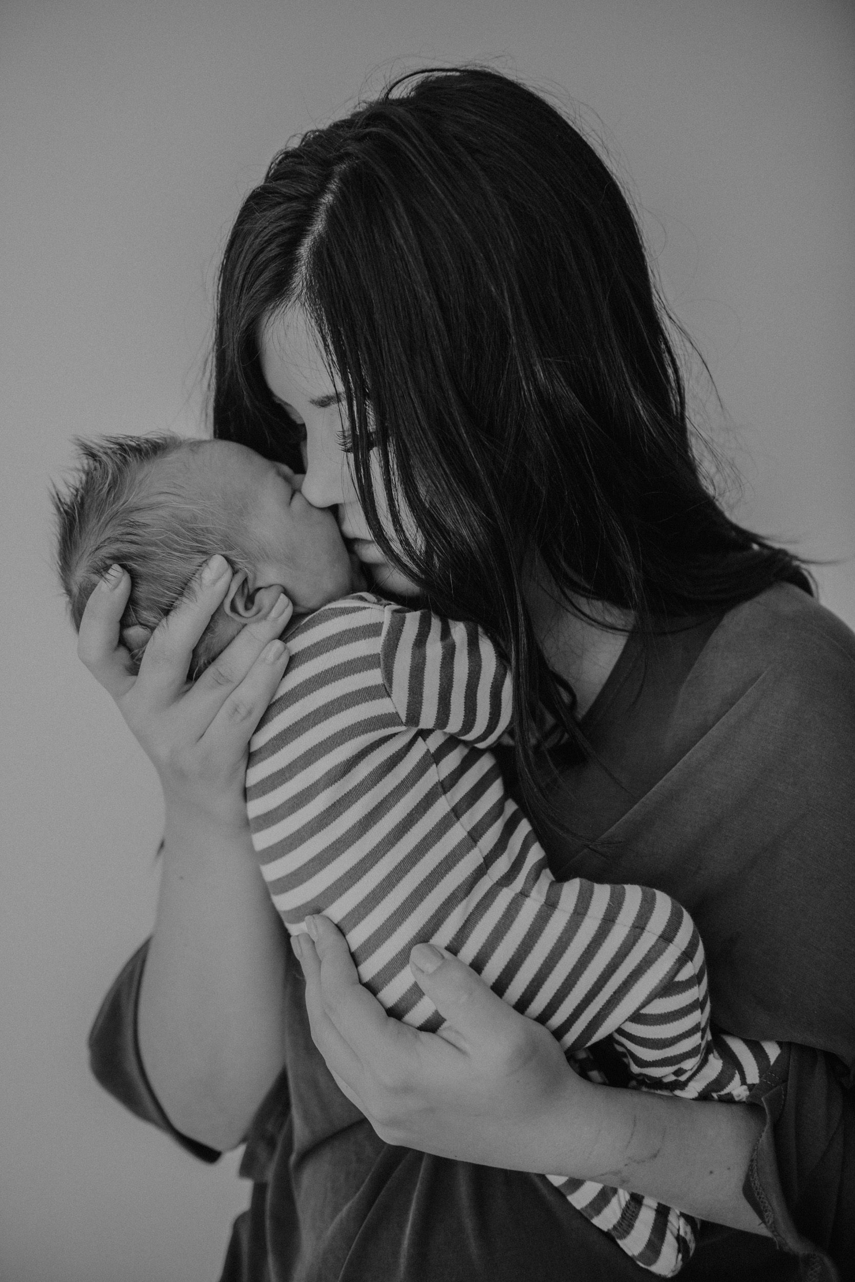 newborn boy in striped onesie being held by mom