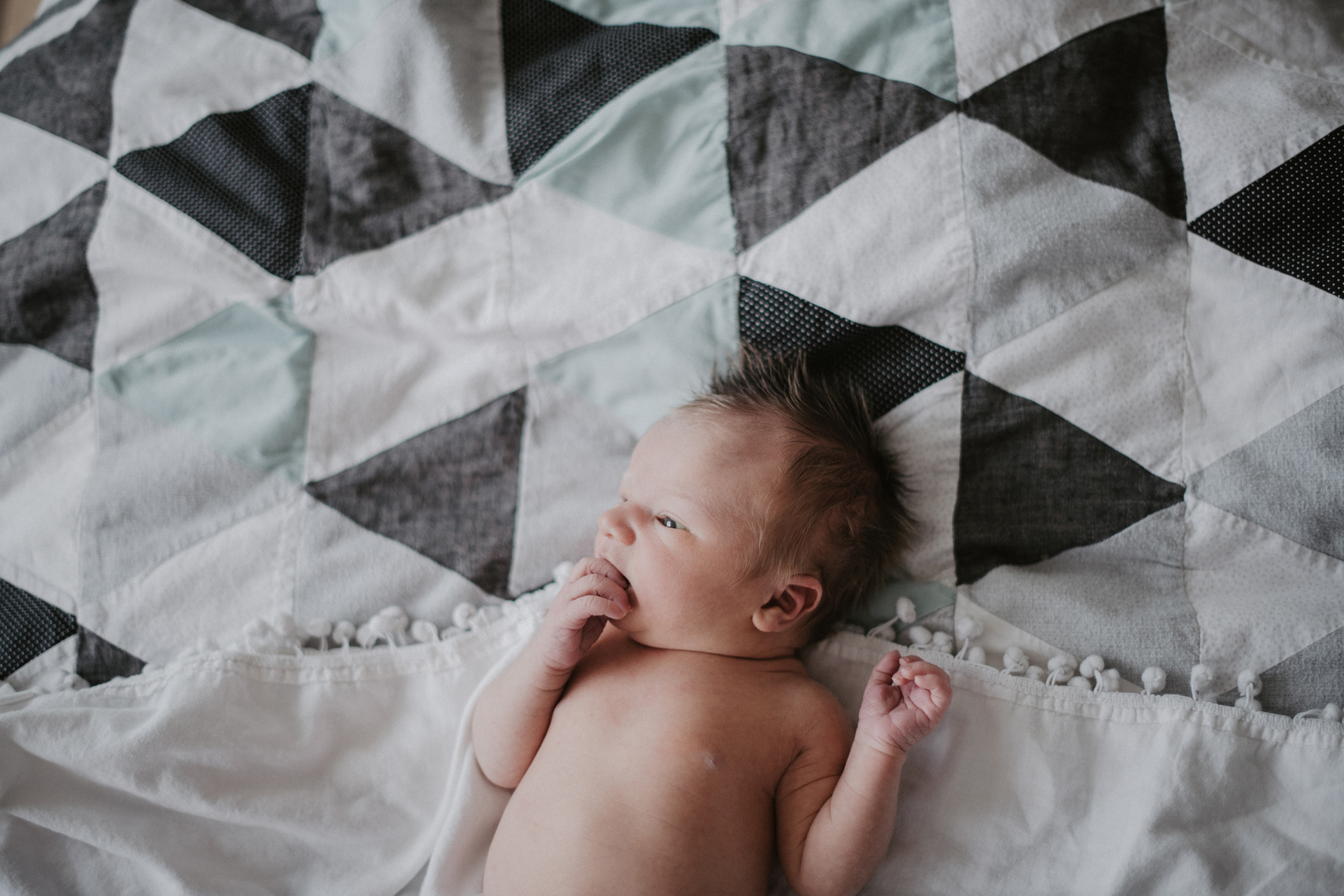 newborn baby boy on triangle and pom pom quilt