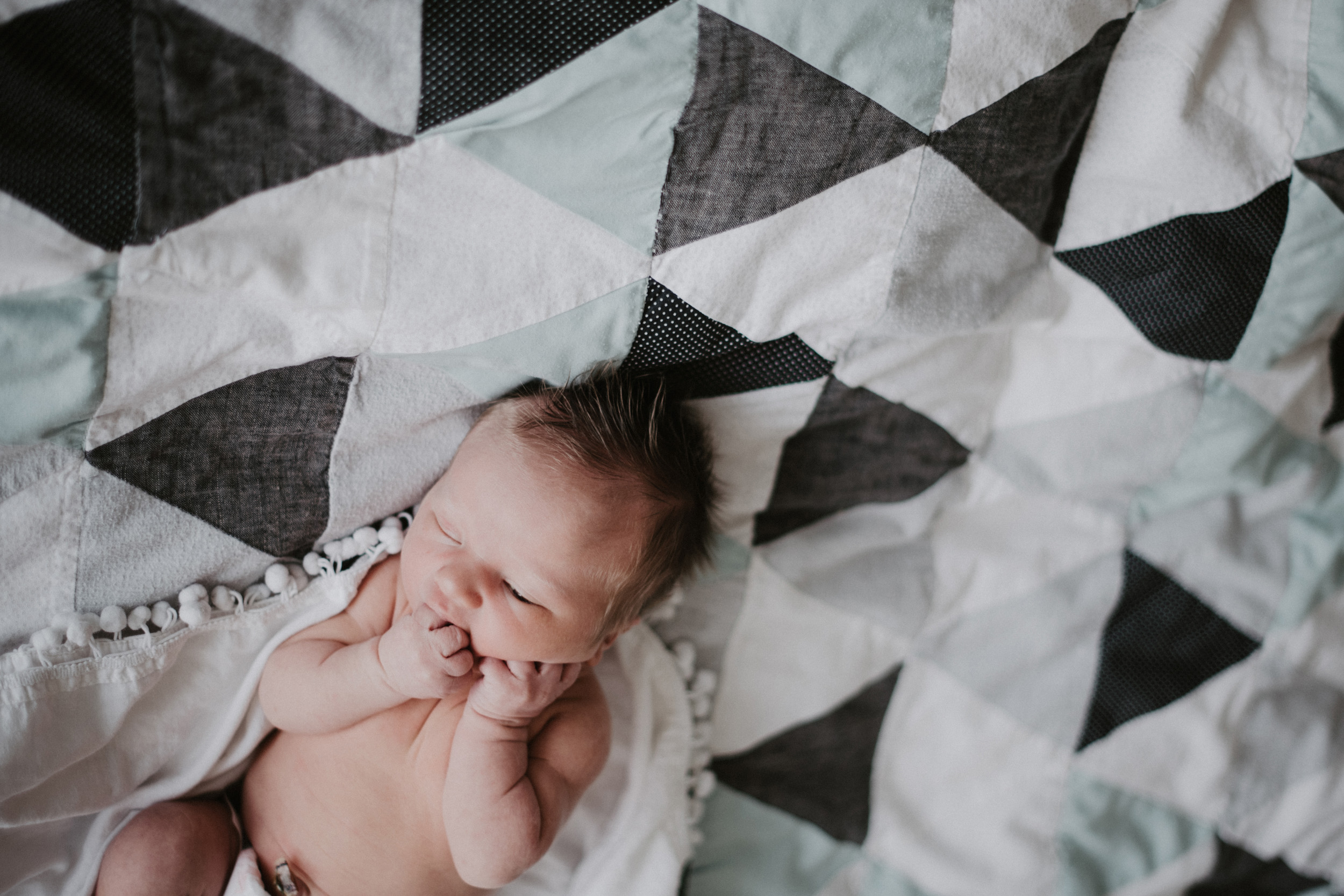 newborn baby boy with hands in mouth on triangle quilt