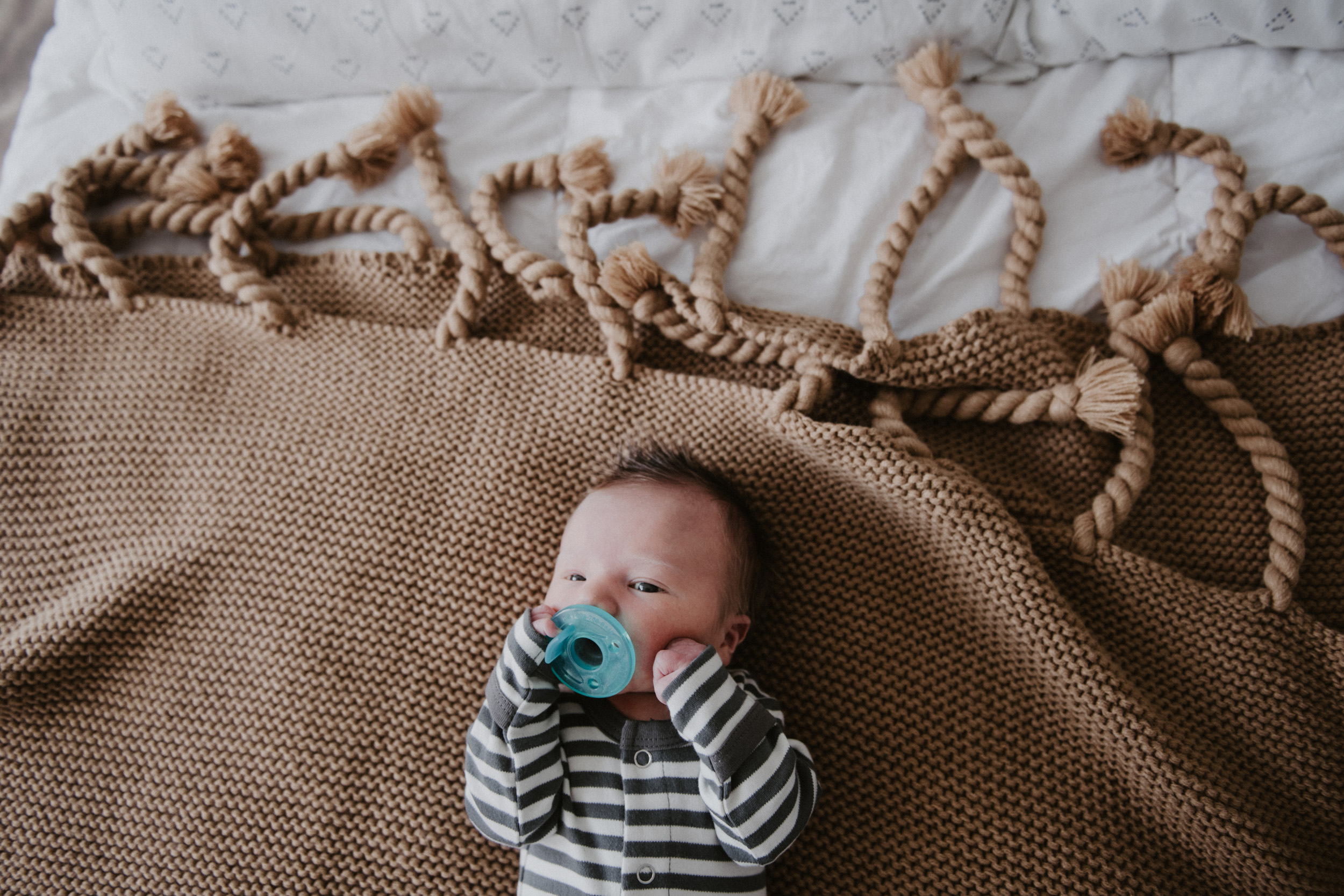 newborn in striped onesie on brown blanket with binkie