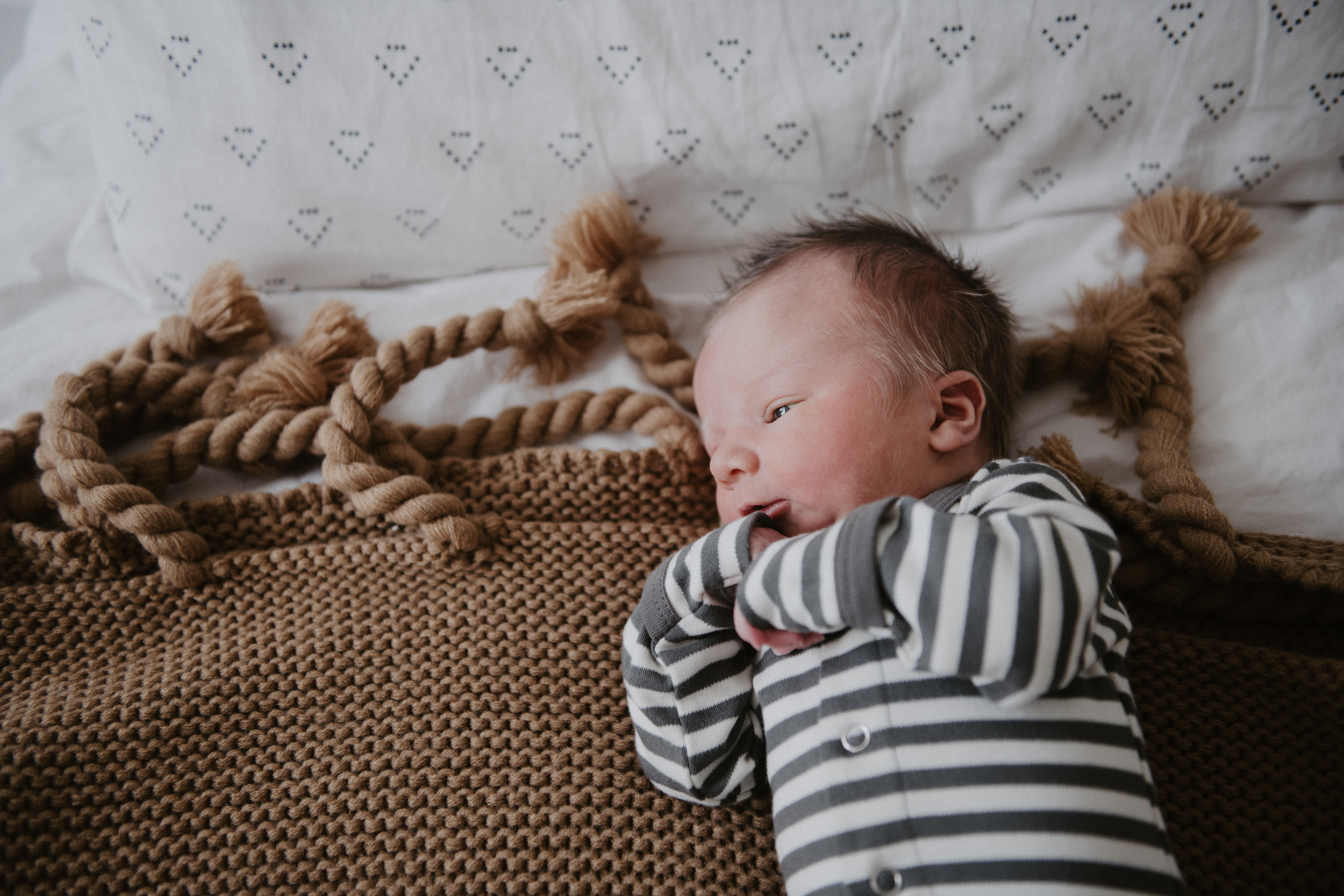 newborn in striped onesie on brown blanket 