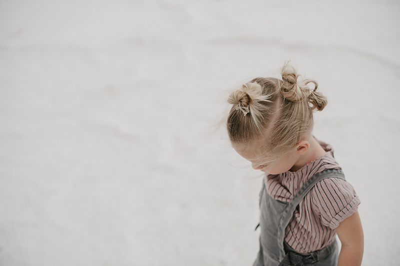 toddler in overalls with buns in hair walking on bonneville salt flats