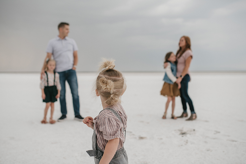 little girl in overalls looking at parents on salt flats