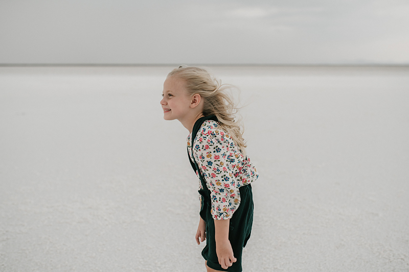 little girl in overall dress with wind blowing through her hair