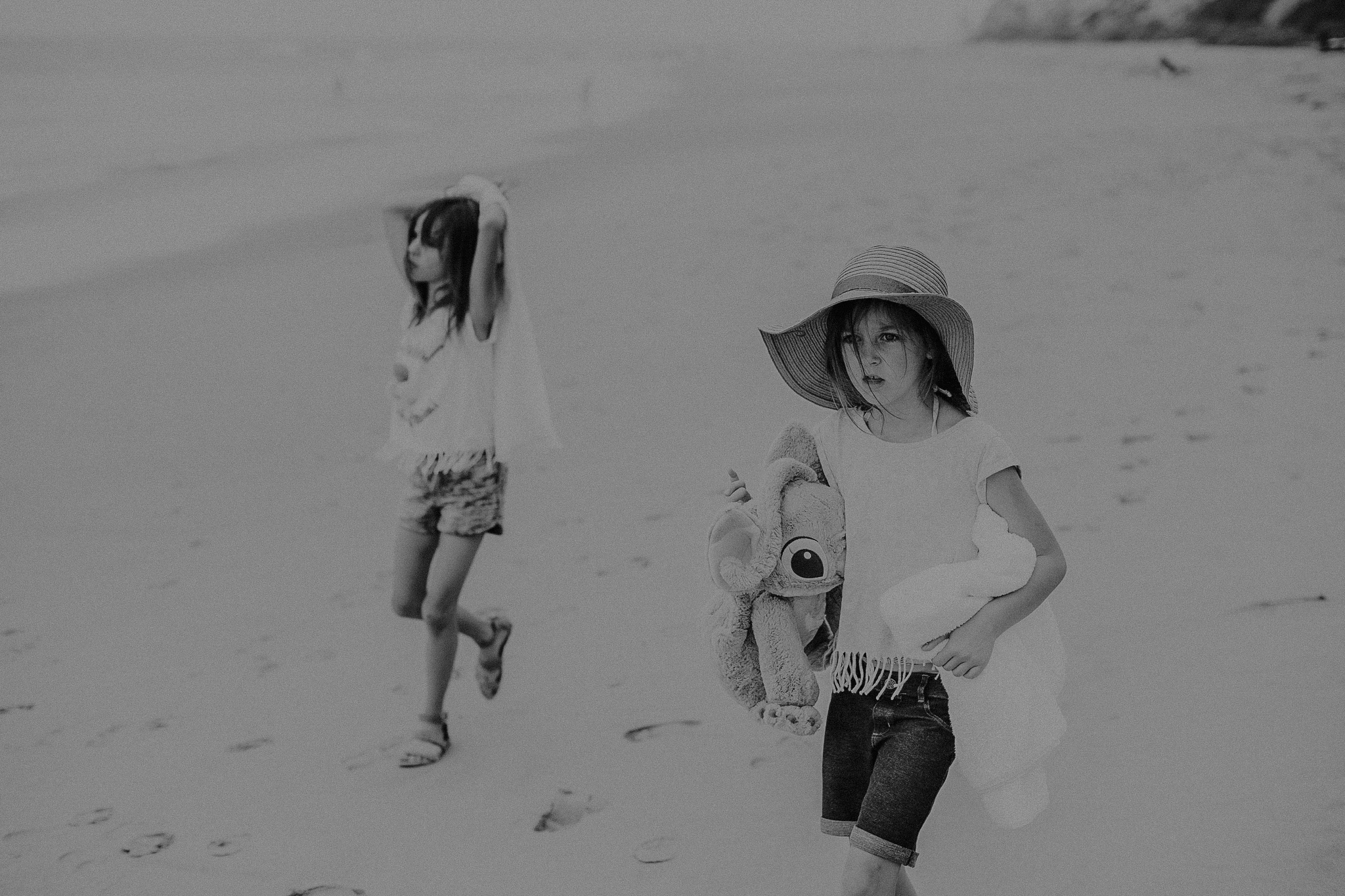 little girl with hat walking along beach with sister