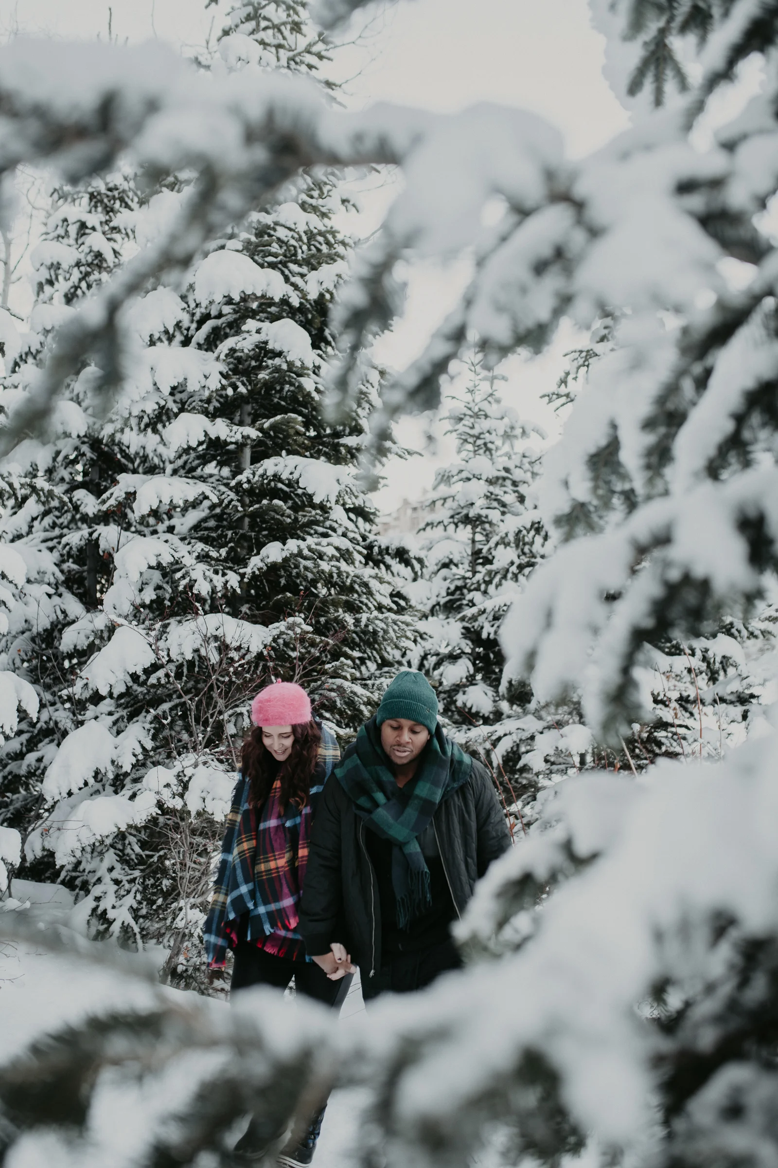 Couple walking through trees in snowy mountains