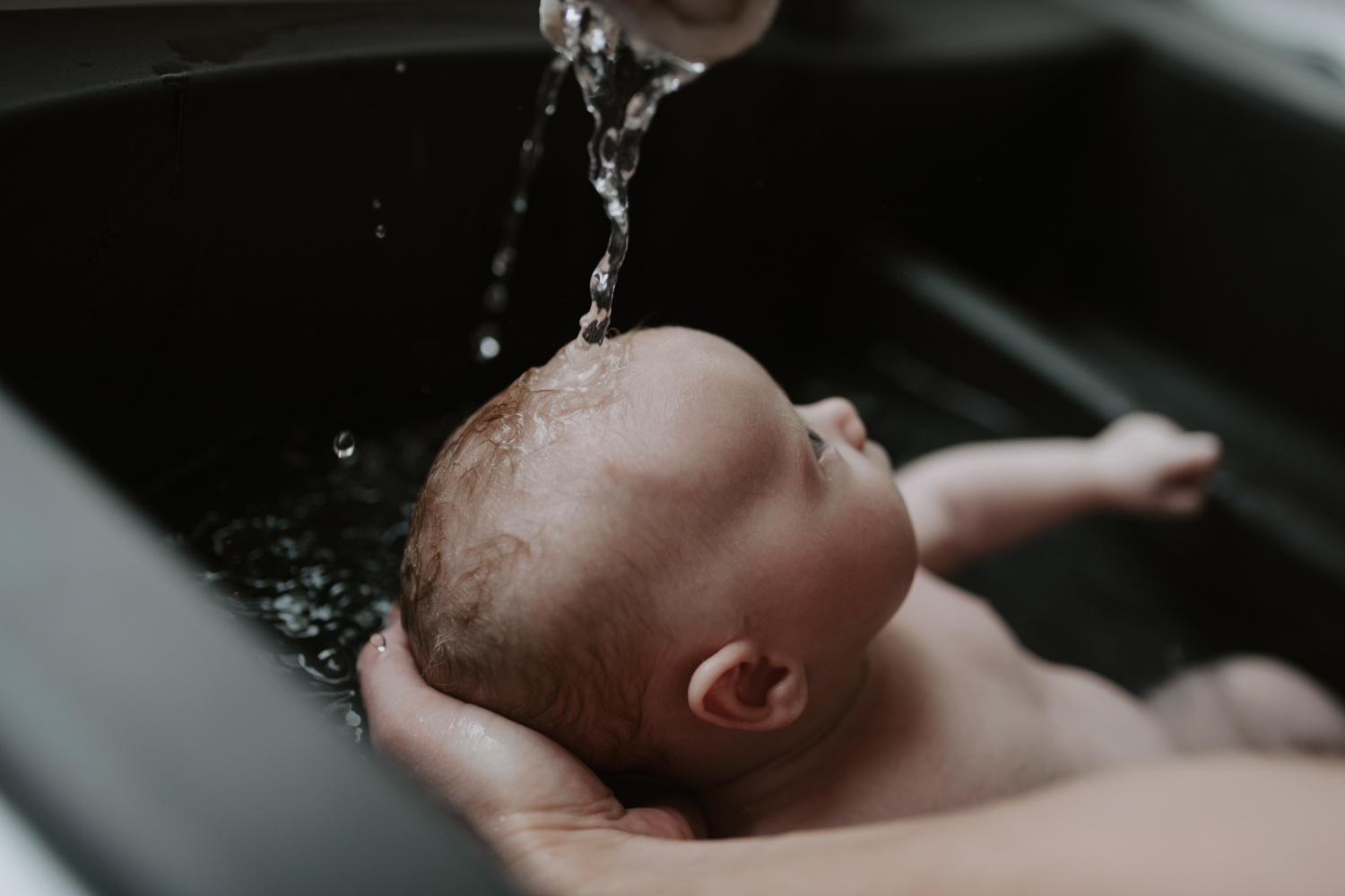 Mother giving newborn baby a bath in a black matte sink