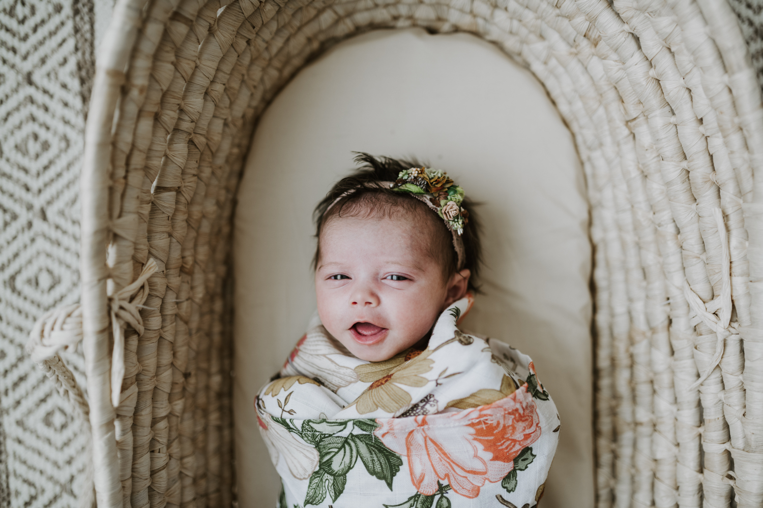 Newborn baby girl wrapped up in flower blanket while laying in bassinet