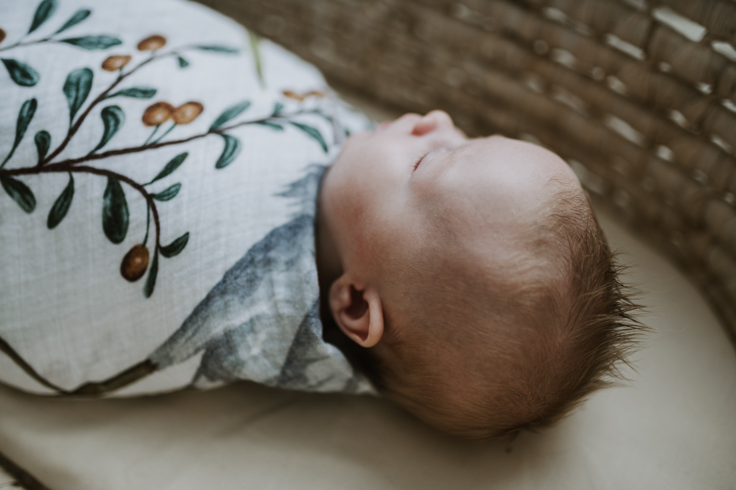 Newborn baby boy wrapped in a leafy blanket while laying in bassinet