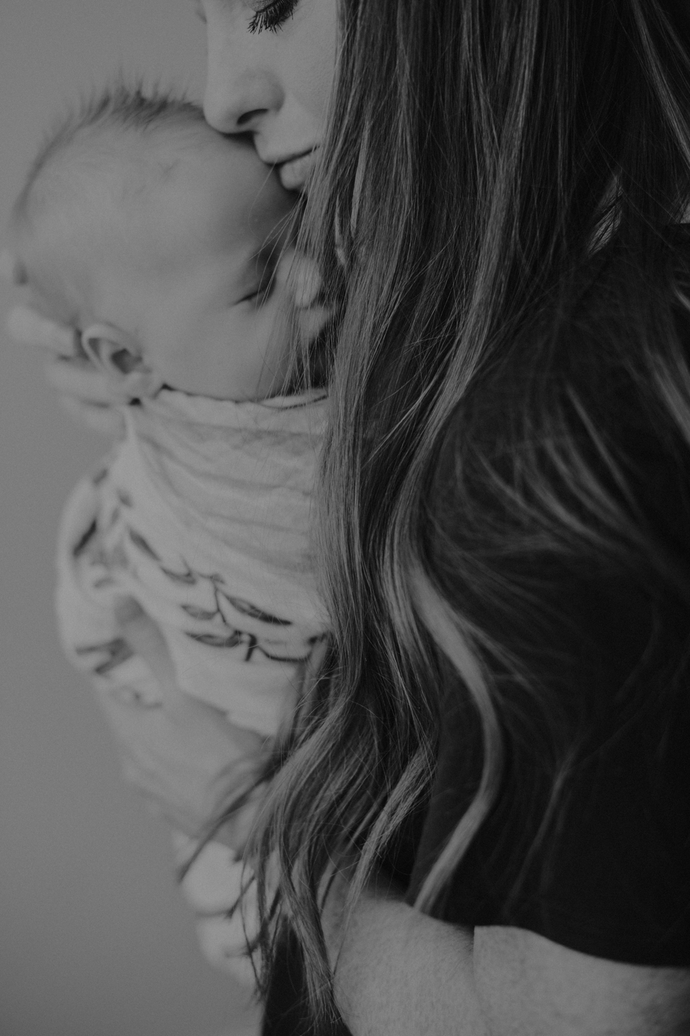 Newborn baby boy being held by mom while getting a forehead kiss