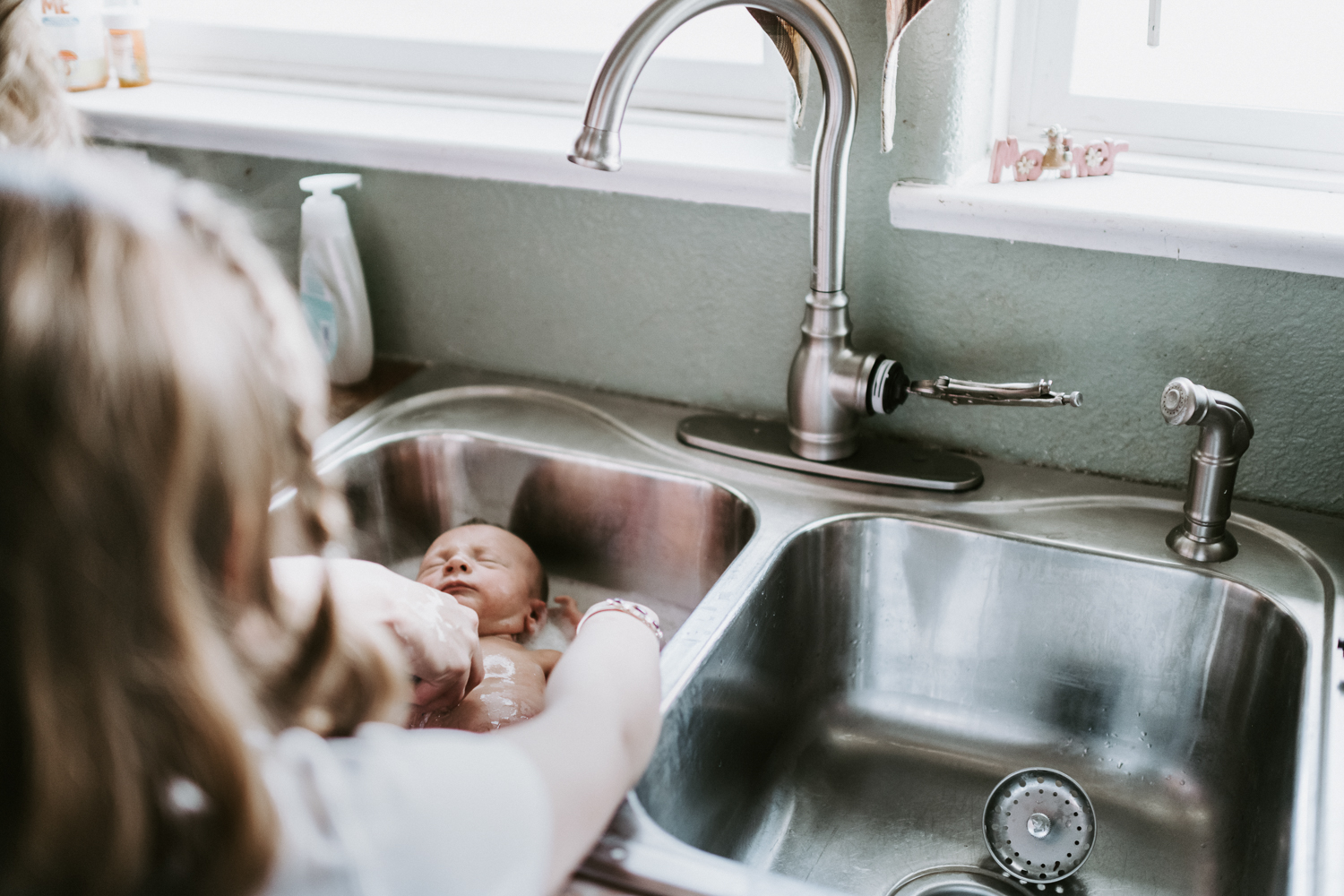 mom giving newborn baby a bath in the sink