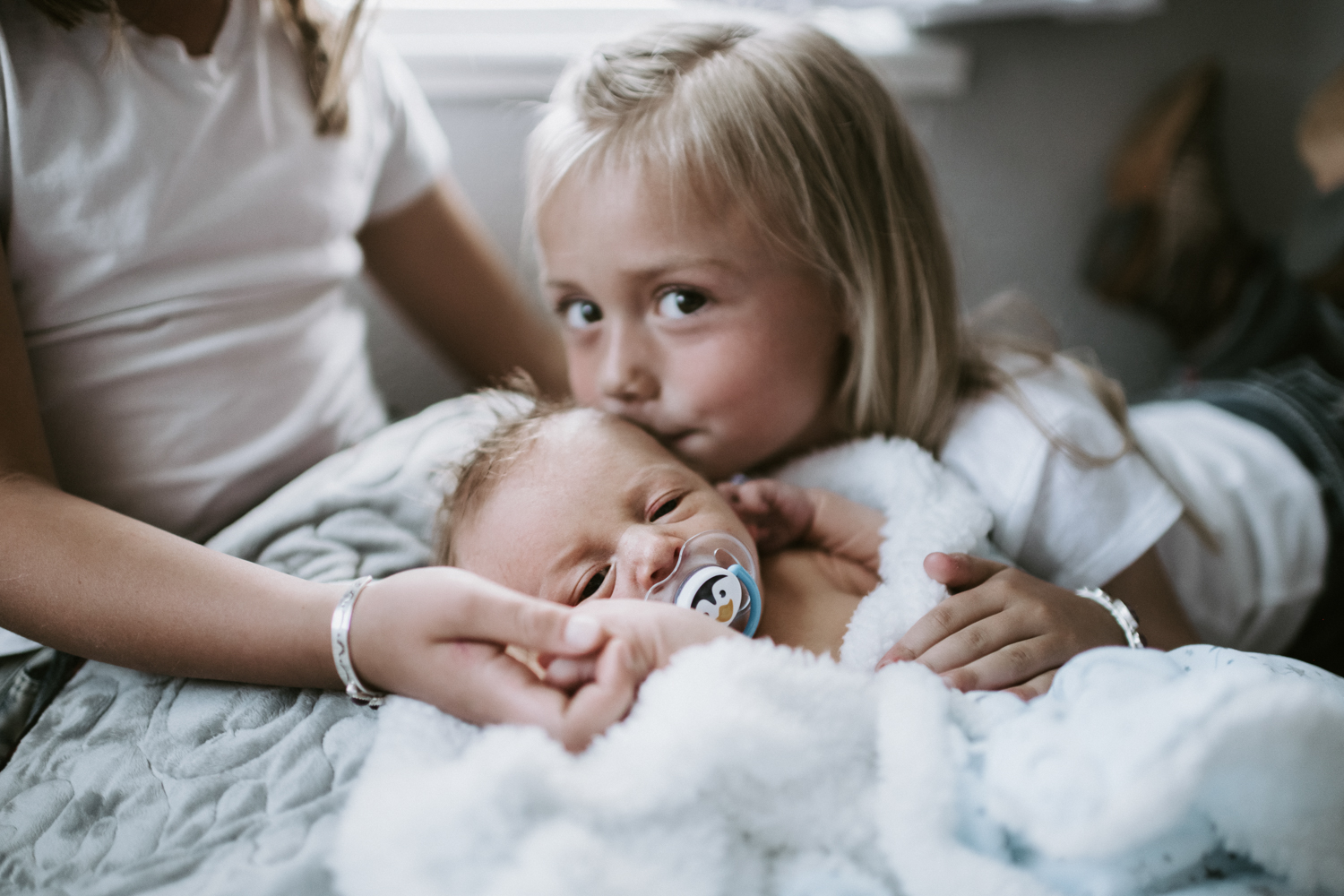 big sister holding newborn baby brother giving him a kiss