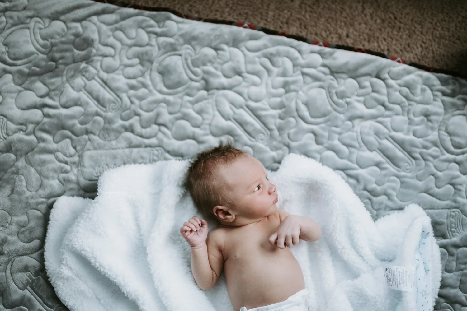 newborn baby boy lying on blanket on floor in nursery