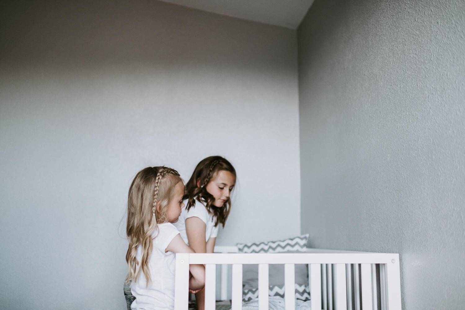 big sisters standing on crib in newborn baby boy nursery