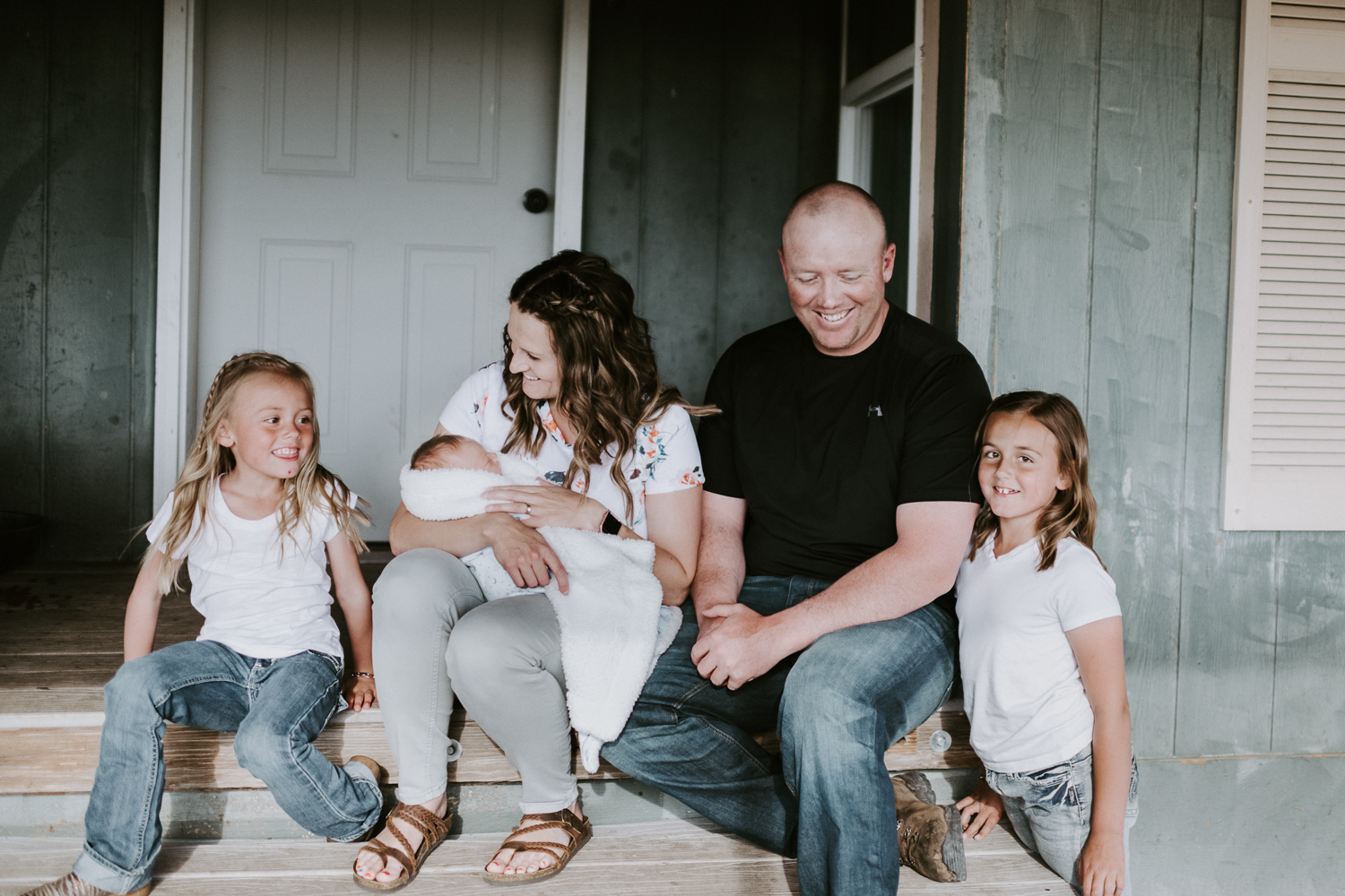 family sitting on front porch with newborn baby boy and daughters
