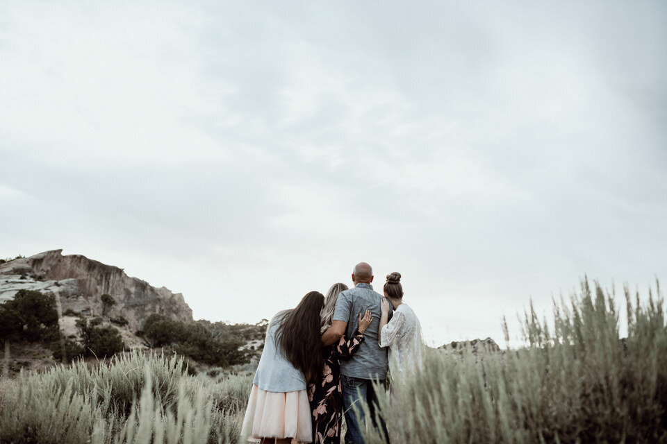 family leaning heads on each other's shoulders looking at mountain standing in field