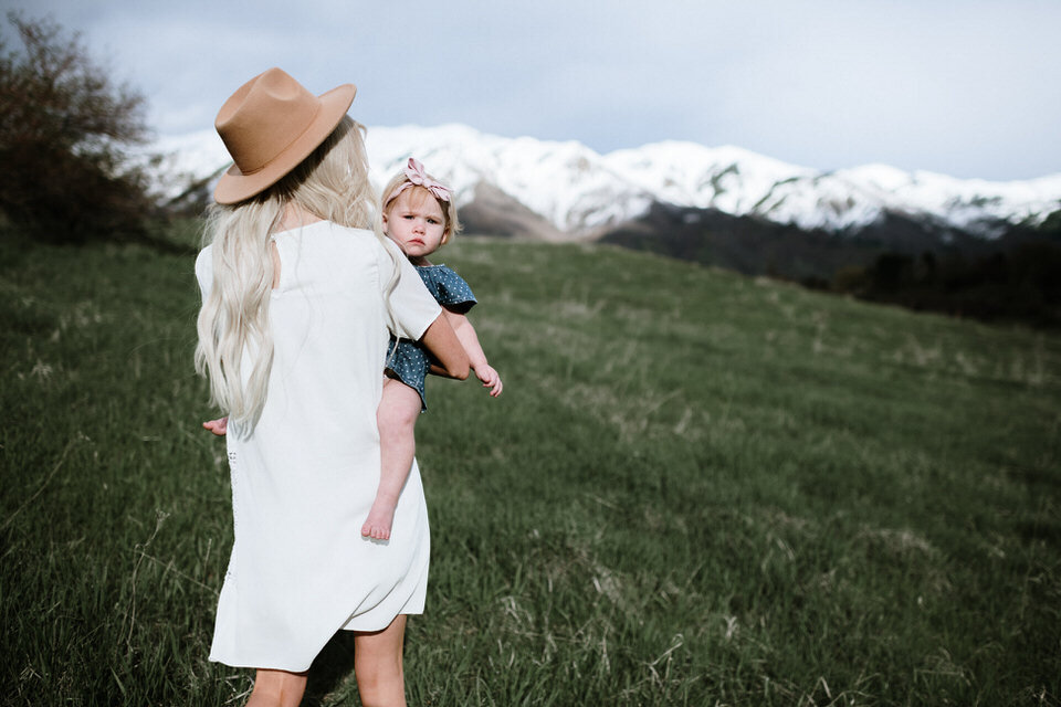 mom holding baby on her hip while walking through grassy hillside