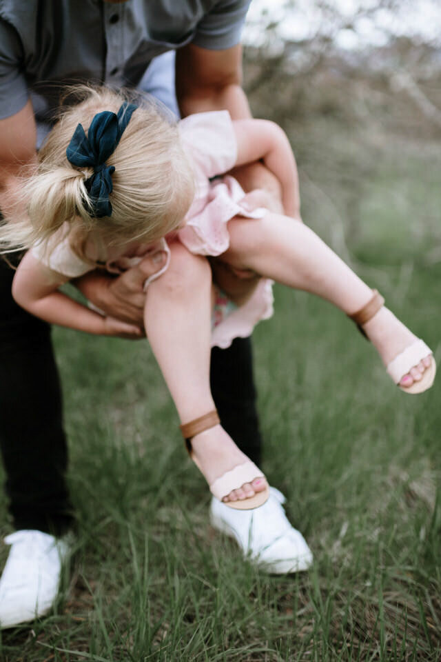 dad swinging little girl in his arms in grassy field